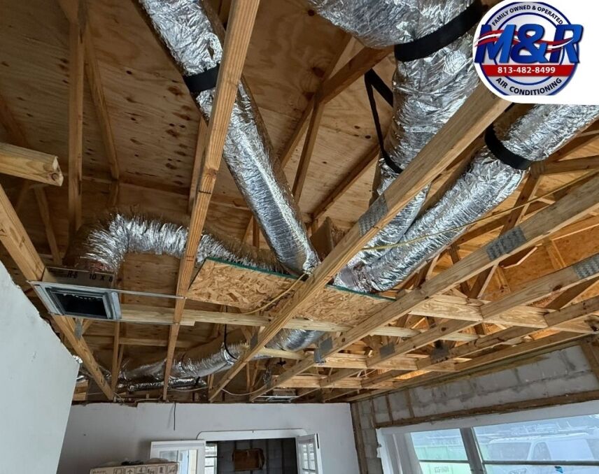 Exposed HVAC ductwork installation in attic framing with new flexible and insulated ducts running through wooden joists during residential construction or remodel.