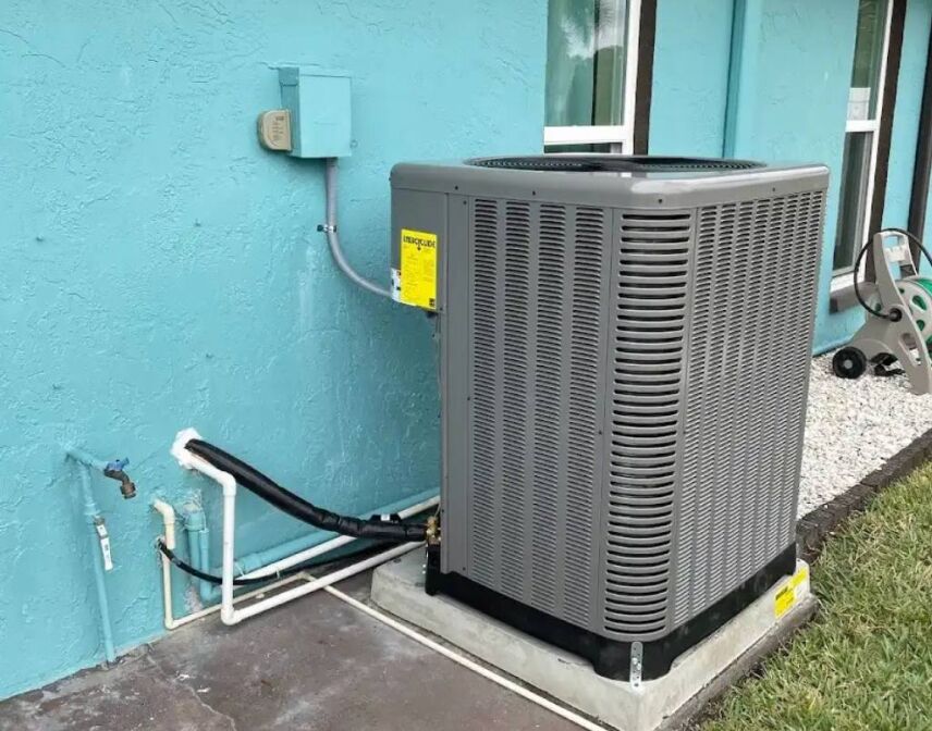 A newly installed residential air conditioning condenser unit on a concrete pad next to a light blue exterior wall with professionally managed refrigerant lines.