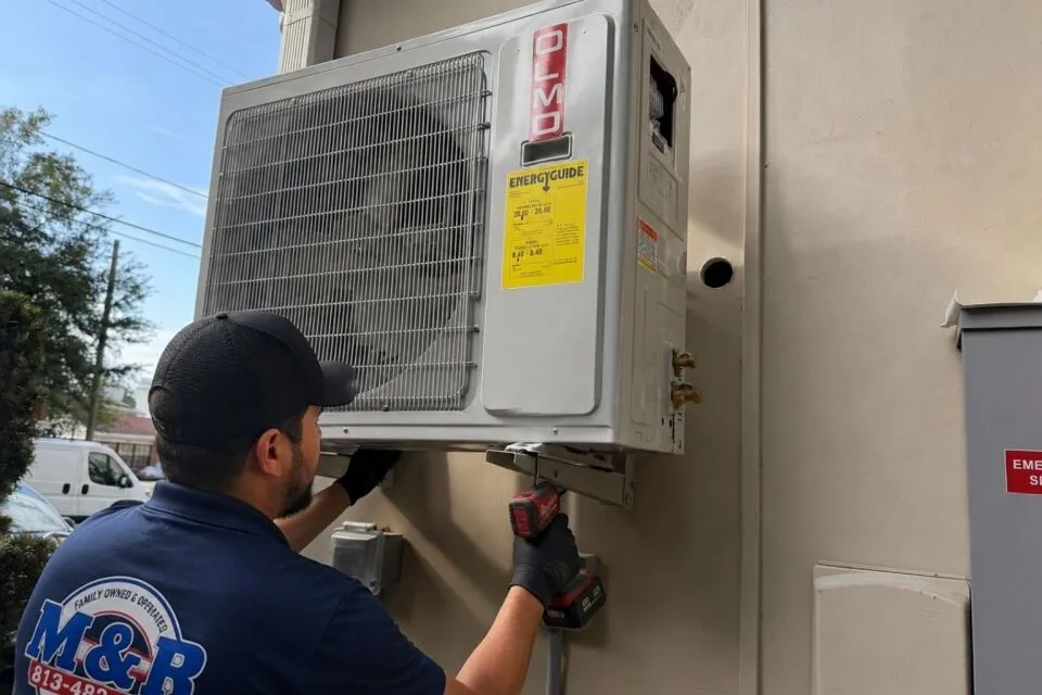 Technician from M&R Air Conditioning installing a ductless mini-split outdoor unit on a residential Florida home, demonstrating proper wall mounting and secure electrical connections for energy-efficient cooling