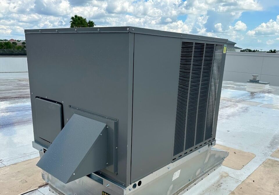 A large commercial packaged HVAC unit secured to a metal roof curb adapter on a flat commercial roof with a white TPO membrane.