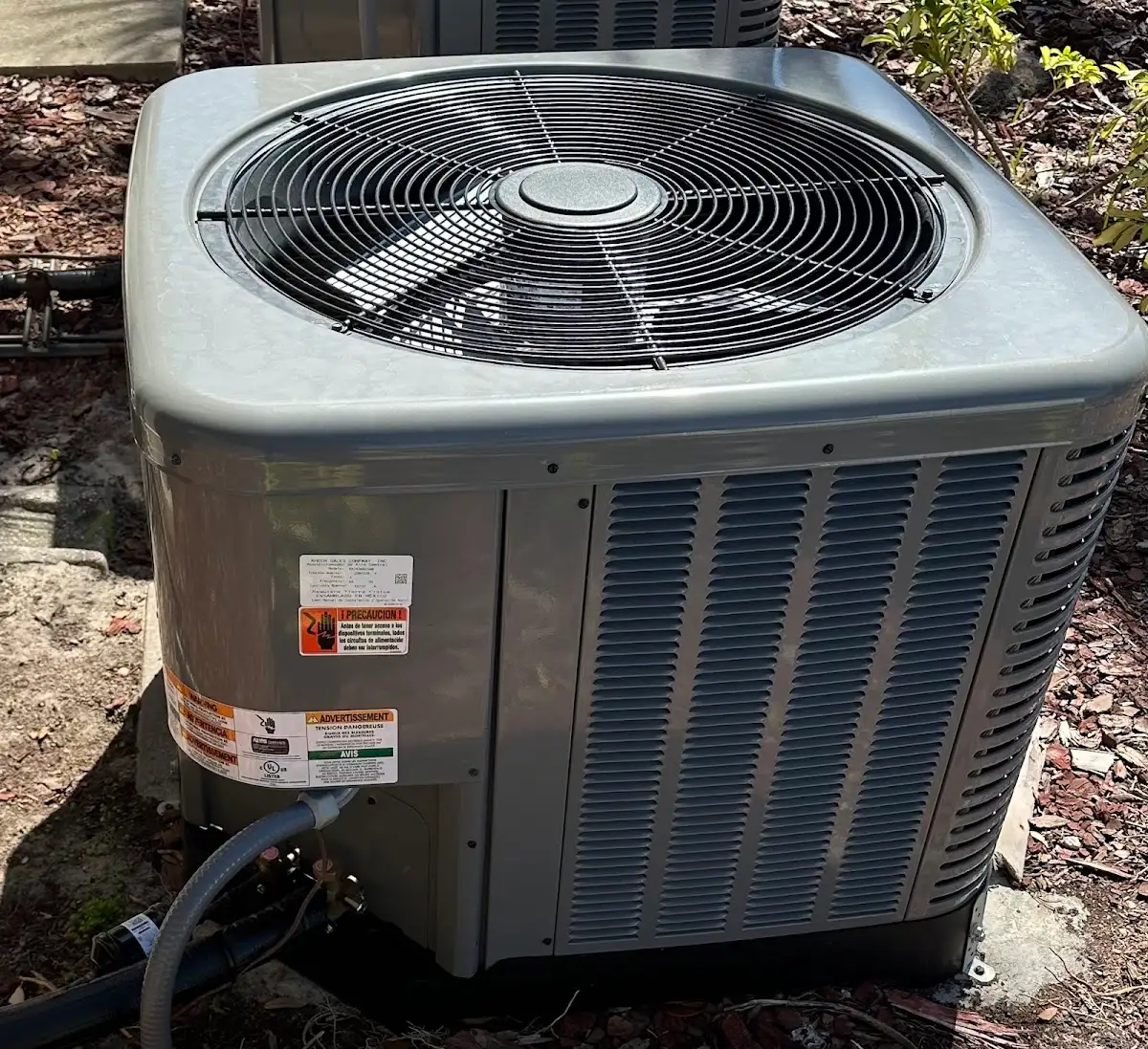 Top-down view of a high-efficiency outdoor AC condenser showing the fan grille and manufacturer safety labels in a residential yard.