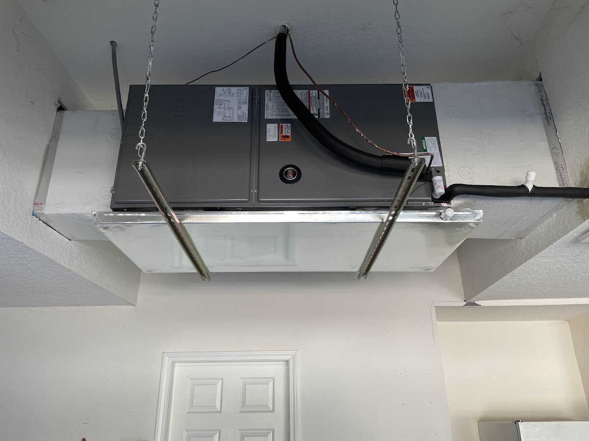 A RUUD indoor air handler unit suspended from garage or attic rafters using heavy-duty chains and an emergency drain pan.