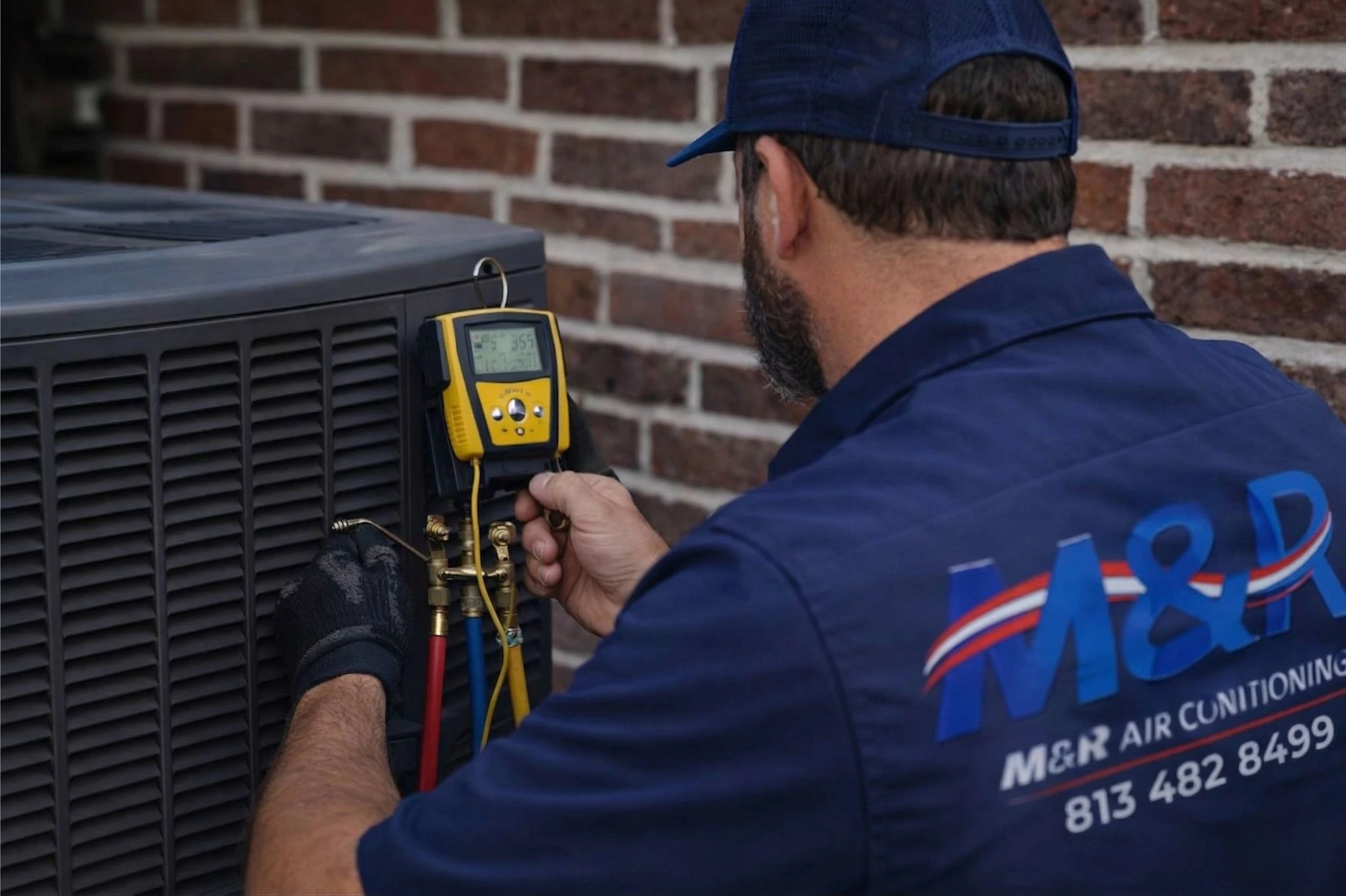 HVAC technician performing AC repair using gauge tools on outdoor air conditioning unit with M&R Air Conditioning branding