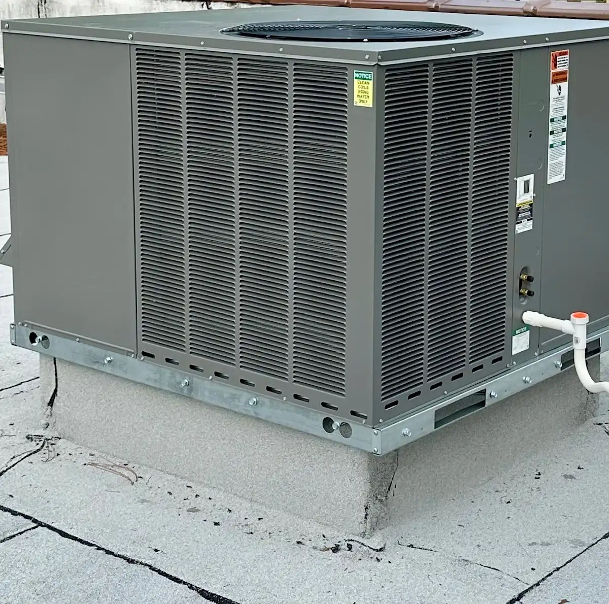 Close-up of a commercial rooftop air conditioner showing the condenser coil intake and a professionally installed PVC condensate drain line.