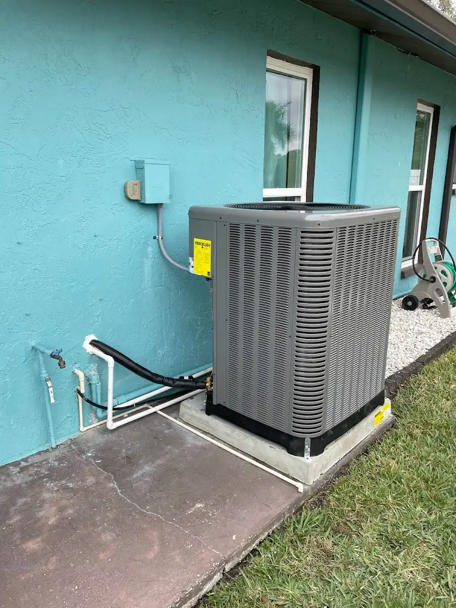 A newly installed residential air conditioning condenser unit on a concrete pad next to a light blue exterior wall with professionally managed refrigerant lines.