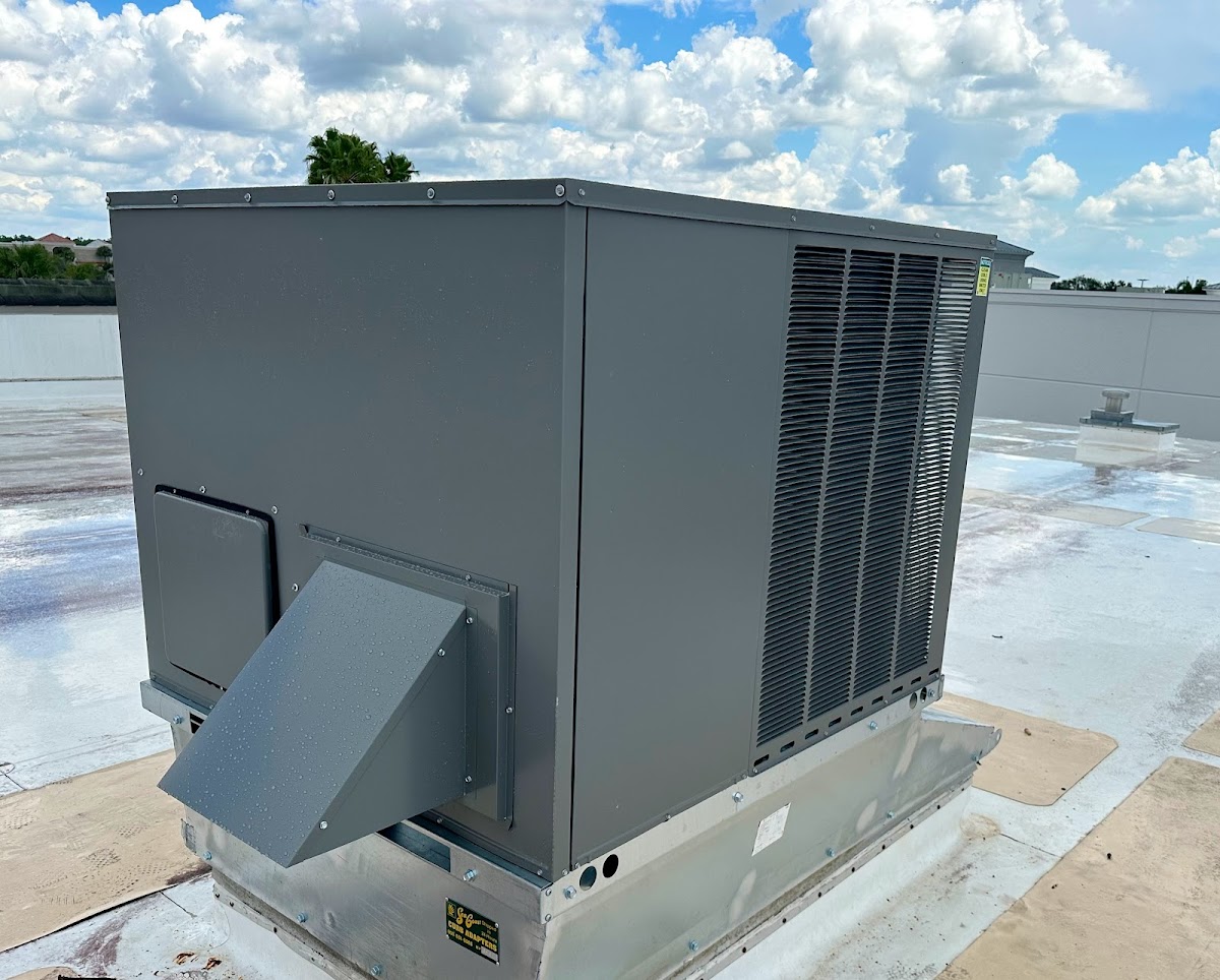 A large commercial packaged HVAC unit secured to a metal roof curb adapter on a flat commercial roof with a white TPO membrane.