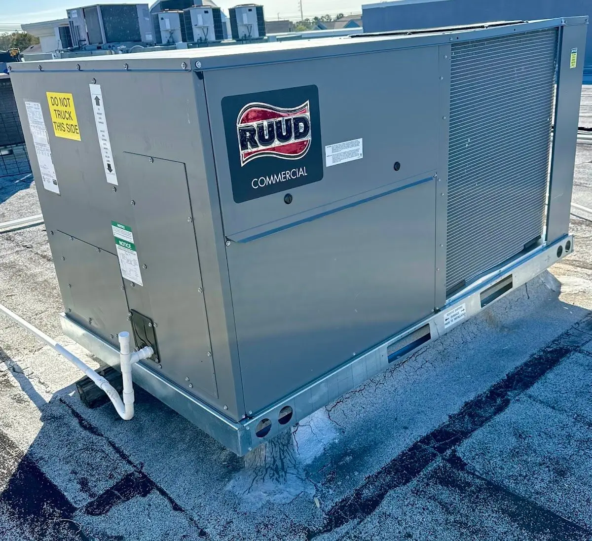 A large RUUD Commercial packaged rooftop unit (RTU) installed on a flat roof with a PVC condensate drain line.
