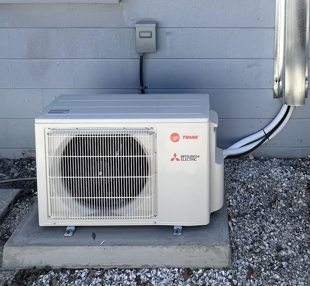 A Trane Mitsubishi Electric ductless outdoor heat pump unit mounted on a level concrete pad with a professional electrical disconnect box.